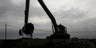 Bagger mit langer Schaufel, der auf einem großen Müllberg thront