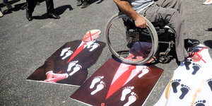 Ein Rollstuhlfahrer fährt über Plakate mit den Gesichtern von Trump, Netanjahu und Prinz Mohammed bin Zayed al-Nahyan.