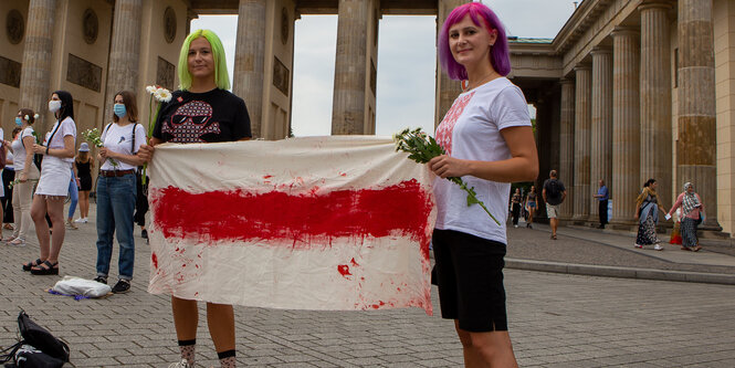 2 Frauen halten eine weiße Flagge mit rotem Streifen hoch