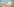 Ein gelber Eimer im Sand, im Hintergrund Wasser