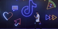 Ein Mann geht an einer Wand entlang, auf der Neonsymbole die App TikTok bewerben