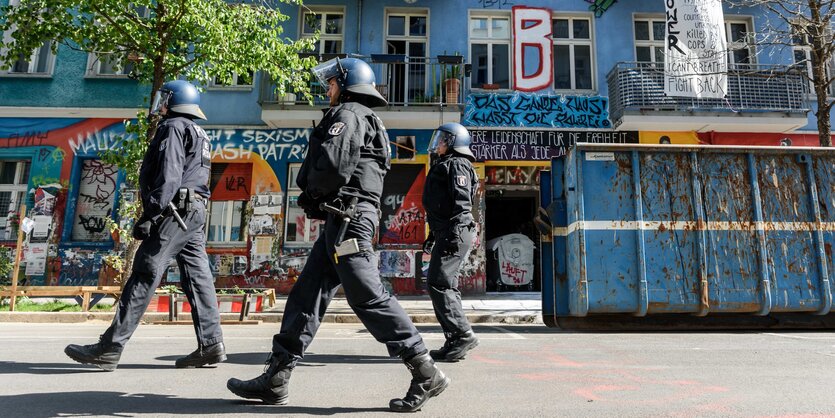 Behelmte Polizisten gehen an einem haus entlang, an dessen Wänden und auf Transparenten Parolen stehen