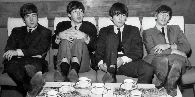 John Lennon, Paul McCartney, George Harrison und Ringo Starr mit angezogenen Beinen auf einem Sofa