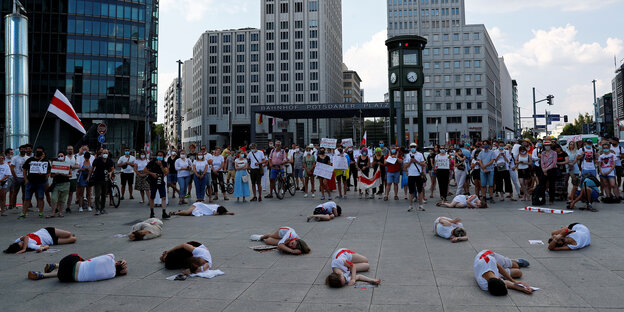 DemonstrantInnen in weiß liegen verstreut auf einem Platz vor Hochhäusern.