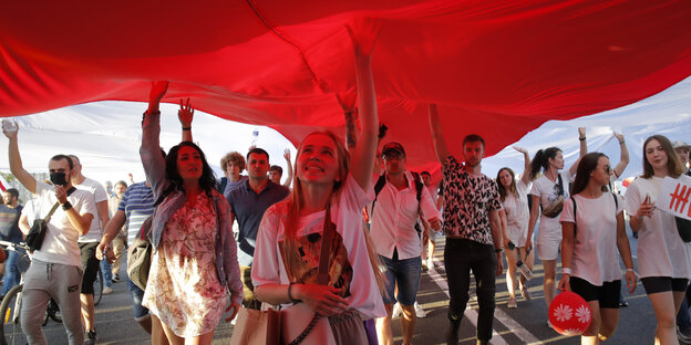 Junge Menschen laufen unter einer riesigen weiß-roten Fahne auf der Straße