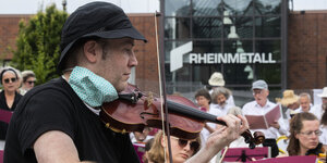 Musiker der Gruppe "Lebenslaute" spielen und singen vor einem Standort des Waffen- und Rüstungskonzerns Rheinmetall.