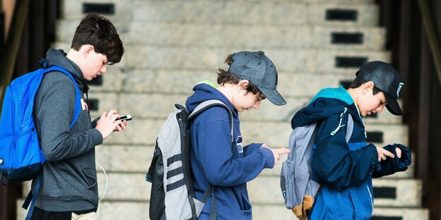 Drei Jugendliche gehen hintereinander die Straße entlang und starren auf ihre Smartphones