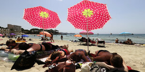 Urlauber liegen am Strand unter Sonnenschirmen mit Erdbeermuster