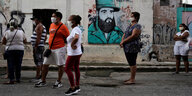 Menschen warten auf einer Strasse in Havanna, im Hintergrund ein Graffiti von fidel Castro