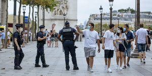 Polizisten und leger gekleidete Menschen auf einem breiten Bürgersteig, im Hintergrund der Triumpfbogen