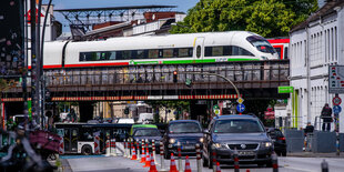 Straßenverkehr in Großstadt, darüber eine Brücke, auf der ein ICE fährt