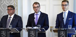 Drei Männer in Anzügen an Mikrophonen