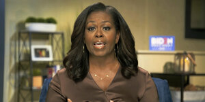 Michelle Obama spricht aus einem Arbeitszimmer in die Kamera. Im Hintergrund ein "Biden"-Werbeschild
