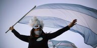 Eine Frau mit Karnevalsmaske und Mundschutz hält argentinische Flagge.