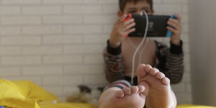 Ein kleiner Junge sitzt im Schlafanzug auf seinem Bett und spielt mit der Nintendo Switch