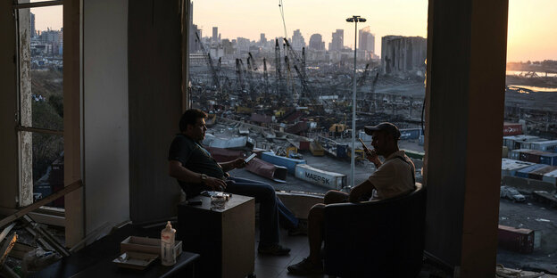 Zwei Männer sitzen in einem zerstörten Gebäude, gegnüber vom Hafen
