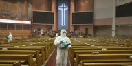 Person in Schutzanzug mit Desinfektionsgerät in leerem Kirchsaal.