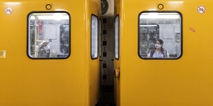 Zwei Menschen mit Mundschutz hinter den Fenstern zweier U-Bahn-Wagons