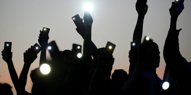 Schattenriss von Menschen die ihre Smarthones in die Luft rechen und als Taschenlampen benutzen