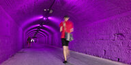 Patricia Kaersenhouts Beitra "Aorta" - eine junge Frau im kurzen Rock geht durch einen tunnel, der violett ausgeleuchtet ist