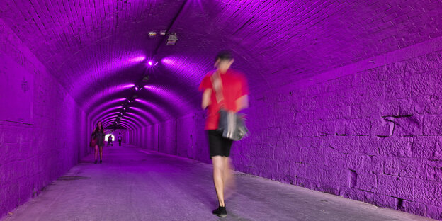 Patricia Kaersenhouts Beitra "Aorta" - eine junge Frau im kurzen Rock geht durch einen tunnel, der violett ausgeleuchtet ist