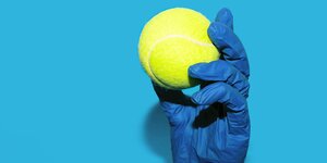 Jemand trägt blaue Medizinhandschuhe und hat einen Tennisball in der Hand