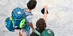 Zwei Schüler stehen mit ihrem Schulranzen und Maske auf dem Schulhof