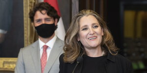 Christya Freeland lächelt, hinter ihr steht Justin Trudeau mit Atemschutzmaske