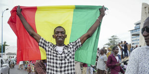 Ein Mann hält die malische Flagge hoch.