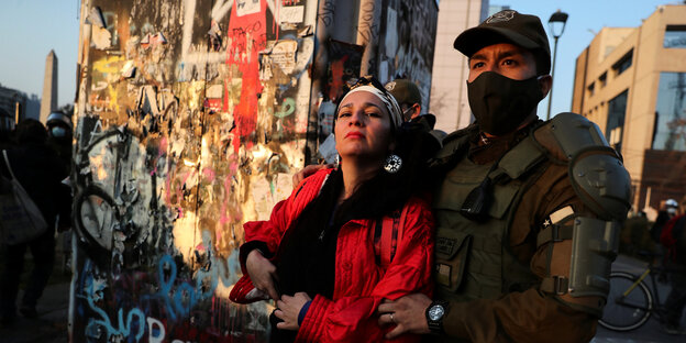 Ein vermummter Polizist hält eine protestierende Frau mit roter Jacke fest