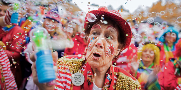 Eine Karnevalistin im rot-goldenen Kostüm erfreut sich an den Seifenblasen vor ihrem Gesicht