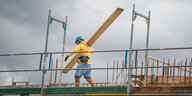 Bauarbeiter mit einem Brett in der Hand, der auf einem Baustellengerüst steht