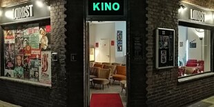 Der Eingang des kleinsten Kinos Deutschlands, des Lodderbast, bei Dunkelheit. Das Wort Kino leuchtet türkis über der Tür, innen sind einige Sitzplatzreihen zu erkennen