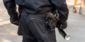 ein Polizist mit Pistole am Halfter und Pfefferspray in der Hand
