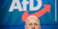 ein Mann mit Glatze und Brille vor dem Logo der AfD