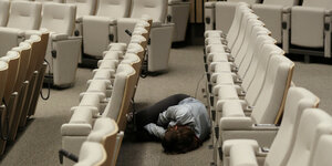 Eine Frau liegt zwischen Stuhlreihen schlafend auf dem Boden