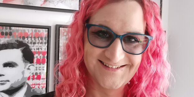 Eine Frau mit rosa Haaren und großer Brille lächelt in die Kamera