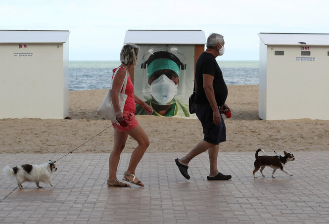 Ein Paar mit Hunden und Masken auf einer Strandpromenade