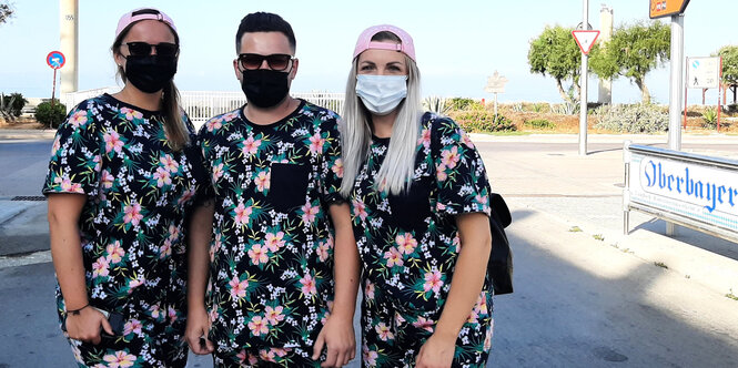 Zwei junge Frauen und ein Mann tehen im Partnerlook - schwarzes Hemd mit rosa Rosen - in Mallorca auf der Straße