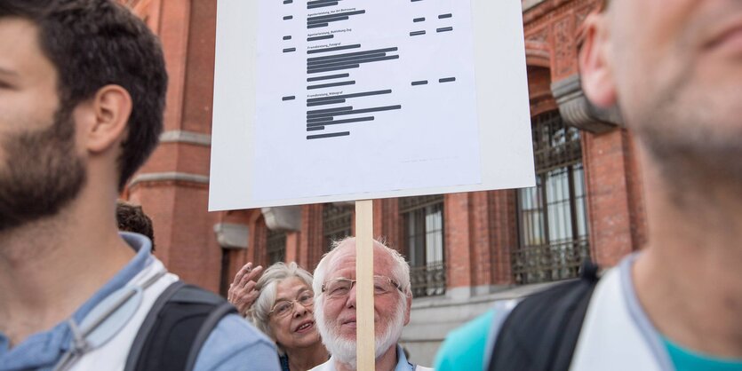 Menschen halten ein Plakat mit geschwärzten Textstellen hoch