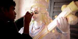 Ein Mann bemalt das Gesicht einer Statue der hinduistischen Göttin Saraswati