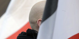 En Mann mit geschorenem Kopf steht zwischen schwarz-weiß-roten Fahnen während einer Demonstration von Rechtsextremen. D