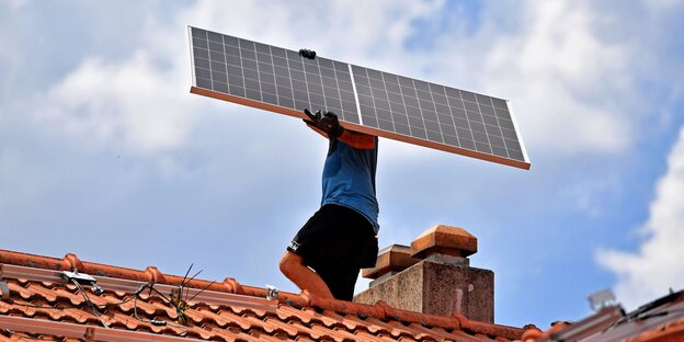 Ein Arbeiter traegt ein Solarpanel,Solarmodul auf ein Dach eines Wohnhauses