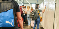 Eine Frau fotografiert mit ihrem Handy den QR-Code ab, der auf dem Informationsblatt steht. Ankommende Passagiere stehen zum kostenlosen Test im Flughafen Schönefeld an.