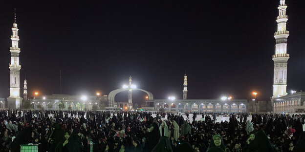 Typische Moschee mit zwei Minaretten, aufgenommen in der Nacht. Vor der Moschee ist eine große Menschenmengezu sehen