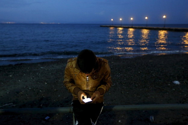 Ein Flüchtling sitzt in Kos, Griechenland, am Strand und bedient ein Handy.