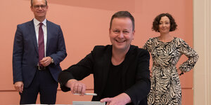 Klaus Lederer unterschreibt lächelnd einen brief