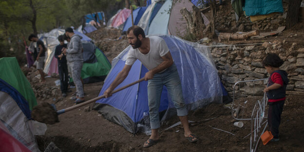 Ein Geflüchteter schaufelt Erde vor einem behelfsmäßigen Zelt auf Samos