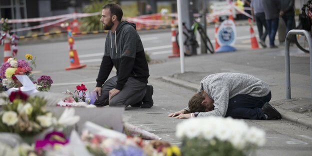 2 Männer knien vor Trauerflor auf einer Straße.
