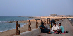 Männer sitzen auf einer Straße am Strand von Sirte